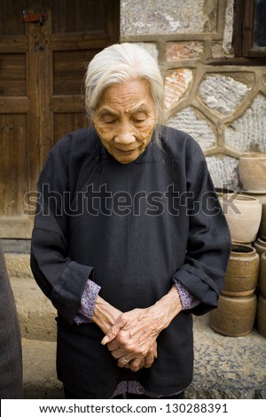 Portrait of elderly Chinese woman standing near her house