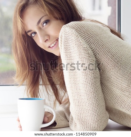 A girl with a charming smile and a glass on a window