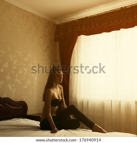 Portrait of beautiful girl sitting on the bed at home near a window at sunset