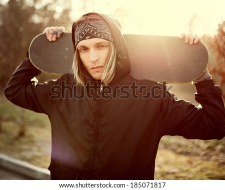 Handsome fashionable guy with skateboard at sunset
