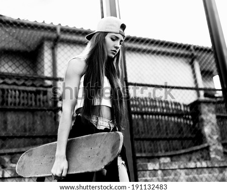 Black and white photo of a girl with skateboard against the sun