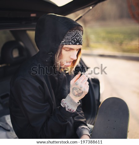 Handsome guy sitting in the trunk of a car and smokes a cigarette