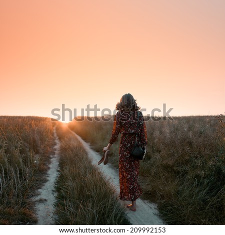 Portrait of beautiful fashionable woman from behind at sunset in the field