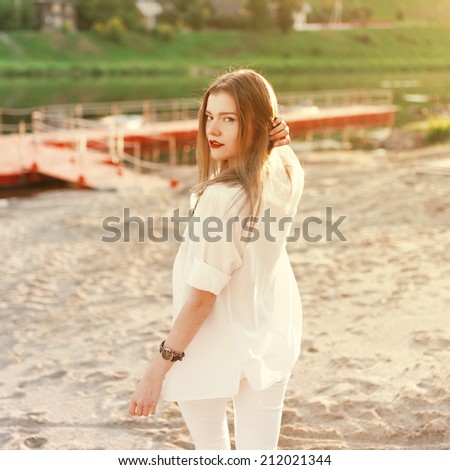 Beautiful cute trendy girl is going in the direction of the pier on the beach on a sunny day and turns