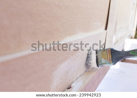 paintbrush painting white on wood fence