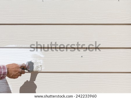 hand worker holding brush painting white on wood fence