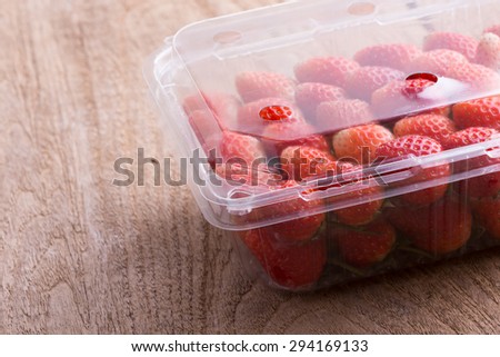 red ripe strawberry in plastic box of packaging on wood table