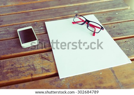 top view of creative workspace with white paper blank and mobile phone on wood table