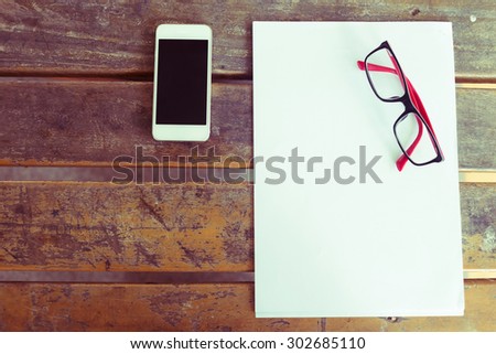 top view of creative workspace with white paper blank and mobile phone on wood table