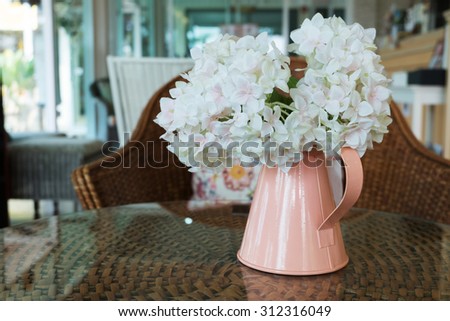 white plastic flowers in pink flower vase on the rattan weave table decorated interior in cafe