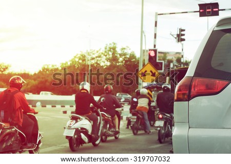 close-up part of tail light of car on urban road with people ride motorcycle stop traffic light on street
