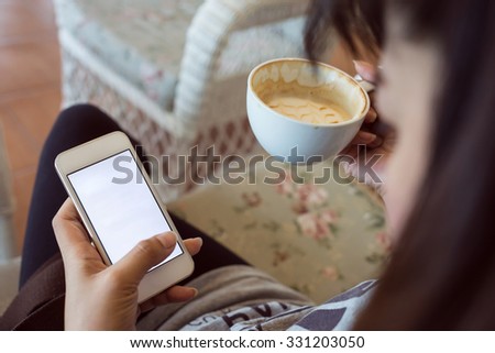 woman drinking hot coffee in cafe and use a mobile phone with blank touch screen, playing social network and shopping online on app smartphone