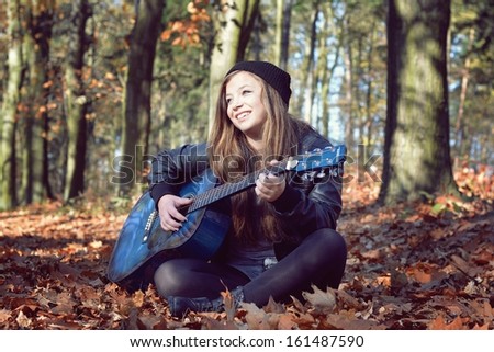 girl playing the guitar in the autumn park