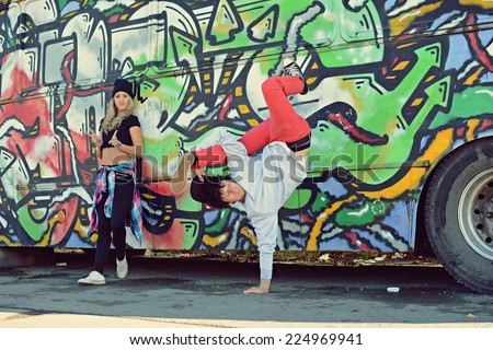 Boy dancing break dance in front of a beautiful girl with stylish bus on the street