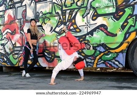 Boy dancing break dance in front of a beautiful girl with stylish bus on the street