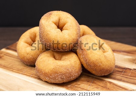 Fresh baked cinnamon donuts staked on a timber board with a black background.