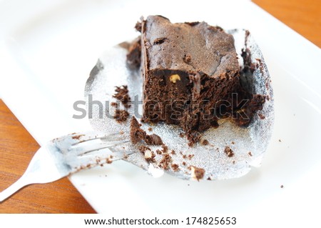 Bitten (eaten) brownie chocolate cake on plate with fork