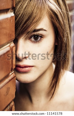 Woman looking behind a brick wall.