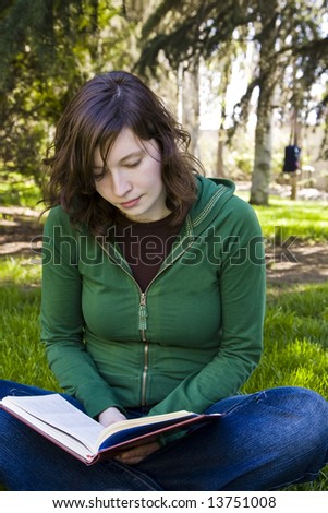 Young student reading on the grass in the park.