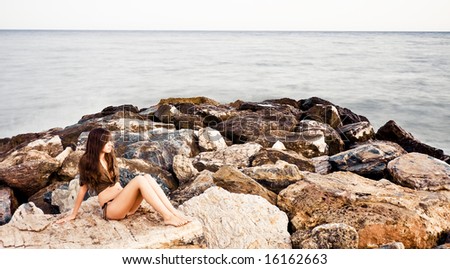Young woman in rocks surrounded by long exposed sea.