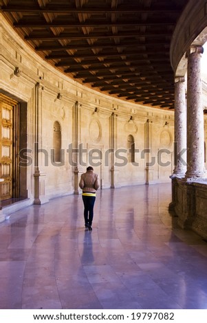 Young woman walking alone in elegant palace corridor.