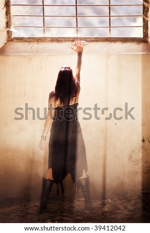 Gothic young woman raising hand towards light.