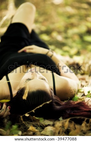 Young beautiful goth girl laying over the foliage.