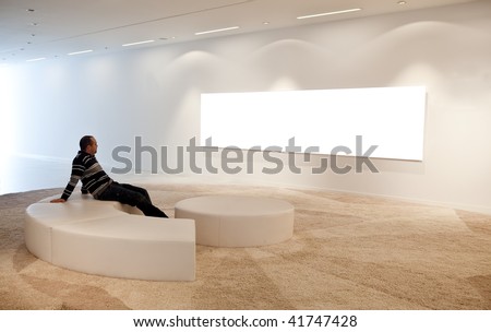 Young sitting man looking at a blank picture on museum wall