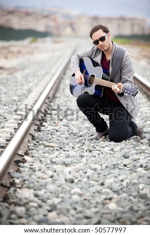 Young handsome musician playing his blue guitar.