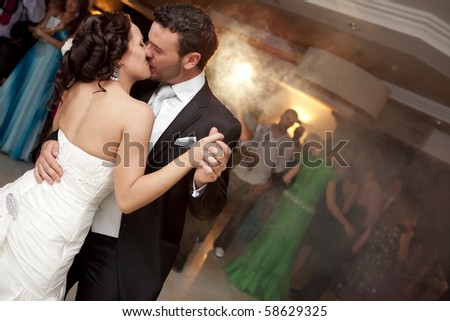 Kissing just married couple dancing in front of their unrecognizable friends.