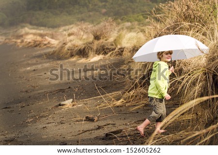 A small child using an umbrella for sun protection down at the beach. Location New Zealand, Kaikoura
