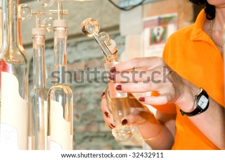 Hands of the woman pouring an alcoholic drink in glasses by means of the glass measured adaptation, inserted into a bottle cork