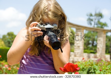 Young  beautiful girl the blonde photographs roses with SLR camera.