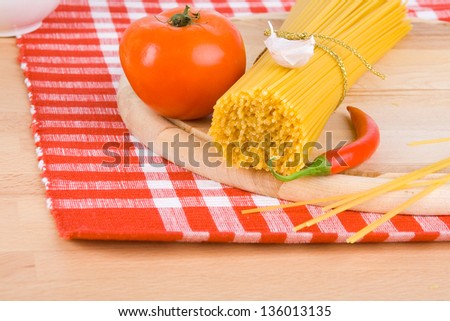 Golden raw dried Italian pasta with other ingredients on kitchen desk.