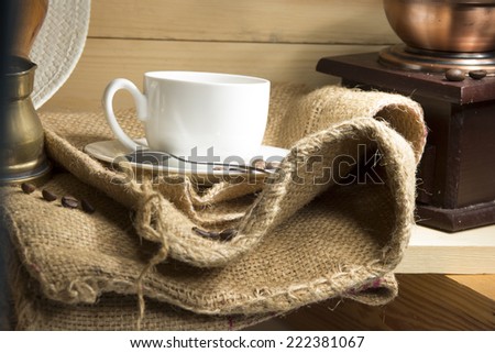 Coffee cup, coffee grinder, coffee brewing arabian Cezve, burlap, coffee beans on a wooden shelf.