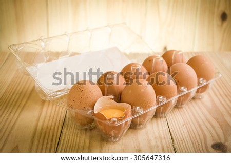 A dozen of eggs in carton, one broken and exposing the yolk