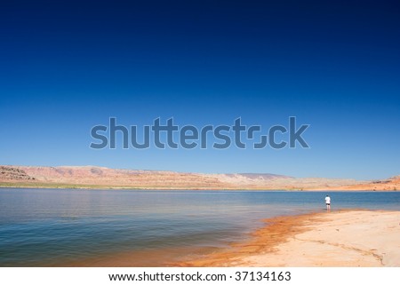 Single person standing alone in a vast barren landcape near a lake.