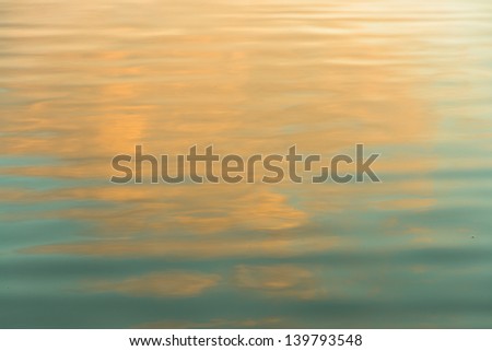 Towering cloud at sunset reflected in moving water.
