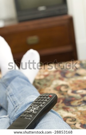 A remote controller sits on the lap of a person laying on a hotel bed.