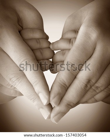 Baby holding mother finger and together form a heart shape