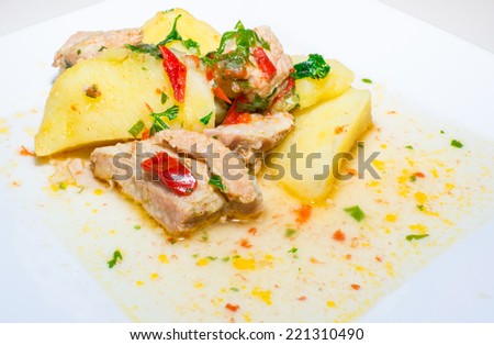 Pork stew with potatoes, onion and red pepper on white serving plate