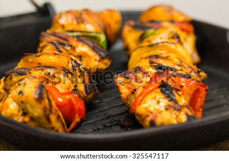 marinated chicken meat skewers with onions and peppers smoking on the grill pan