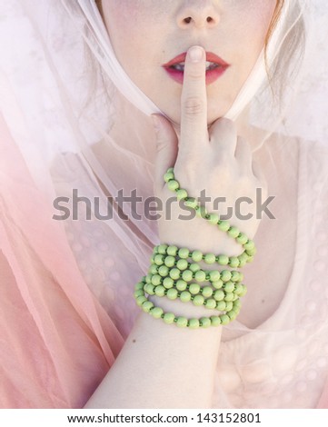 Keep it like a secret. Close up of a sensual woman making a keep quiet gesture putting her finger on mouth. Retro style with veils.