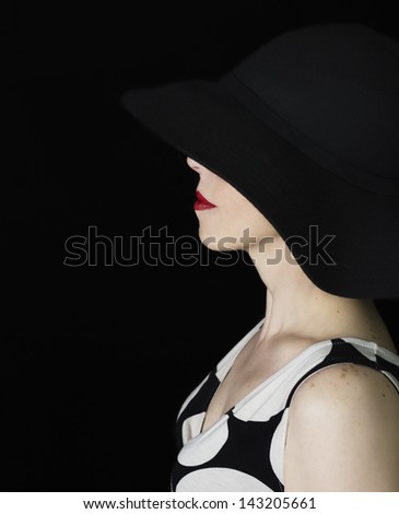 Elegant retro woman wearing a black hat. Only her red lips are visible from under the hat, Black background.