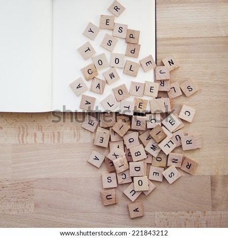 Group of lettered tiles on blank pages. Wooden table.