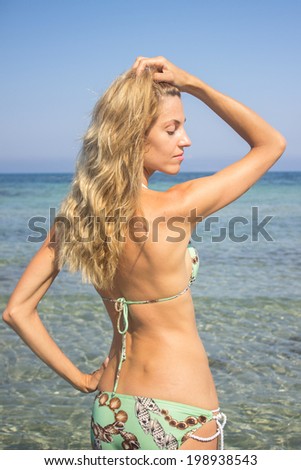 Beautiful blonde woman sunbathing standing in the sea water, side view, torso