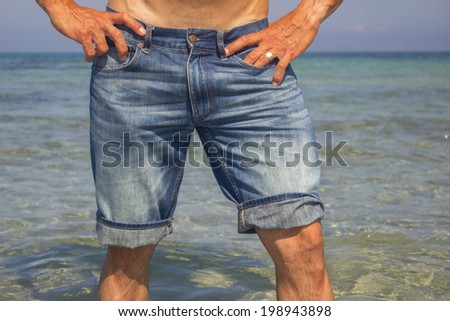 Man wearing jeans shorts standing in the sea water, legs closeup