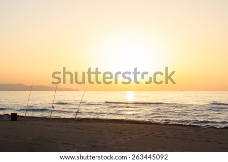 Fish-rods on sea beach at sunset