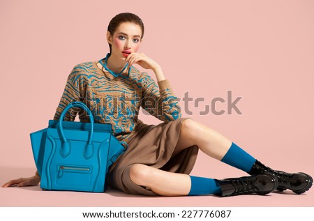 Fashion model in design clothes and blue bag posed on light color background
