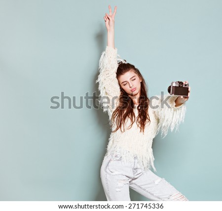 hipster photographer fashion stylish woman dancing and making photo using retro camera. Portrait on blue background in white sweater